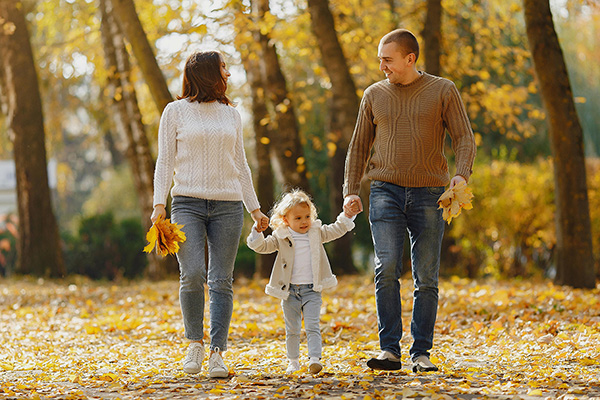 A couple walking hand in hand with their young daughter through autumn leaves